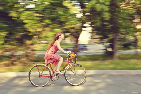 Movimento sfocato. giovane donna in abito va in bicicletta in un parco estivo — Foto Stock