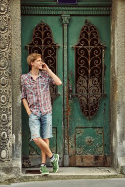 bir binanın eski bir vintage kapı yakınında cep telefonu ile rahat genç adam.