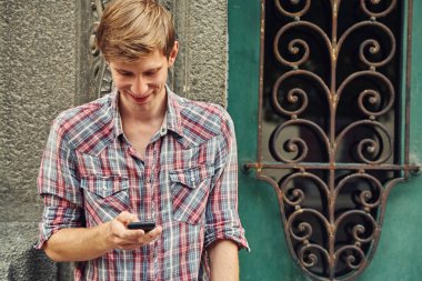 bir binanın eski bir vintage kapı yakınında cep telefonu ile rahat genç adam.