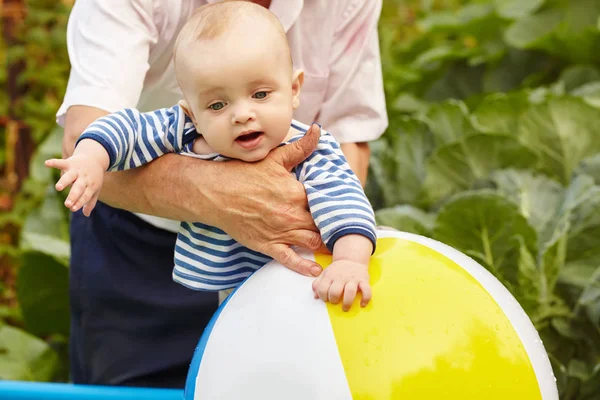 Bébé sur les mains de son père jouant avec la boule gonflable dans une piscine . — Photo