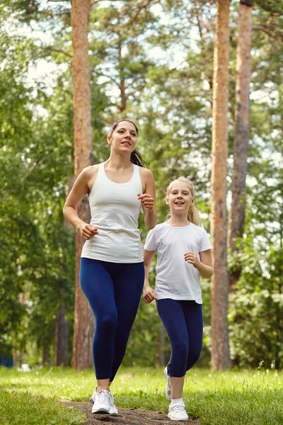 V provozu sportovní matky a dcery. Žena a dítě běhají v parku. venkovní sporty a fitness rodina — Stock fotografie