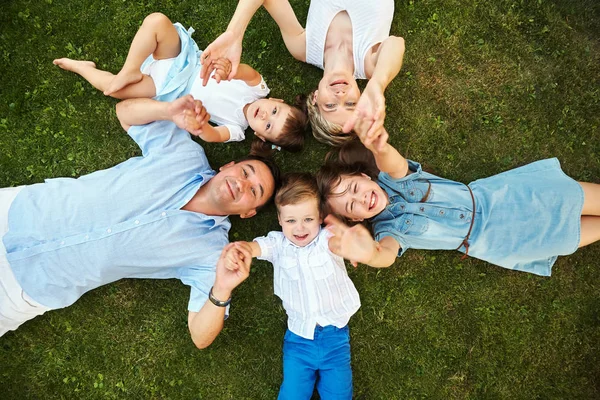 Lycklig lekfull familj som ligger på gräs utomhus. föräldrar med barn på sommaren. Mamma, Pappa och barn — Stockfoto