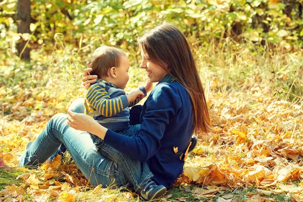Utomhus porträtt av en ung mor med sin baby. Mamma och son i en park på hösten. — Stockfoto