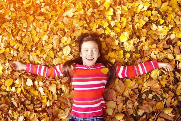 Mooie lachende tiener meisje liggend op gele bladeren in de herfst. Top View. — Stockfoto