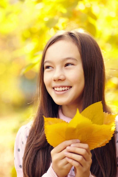 Closeup portret van een mooie lachende tienermeisje met gele bladeren in de herfst. — Stockfoto