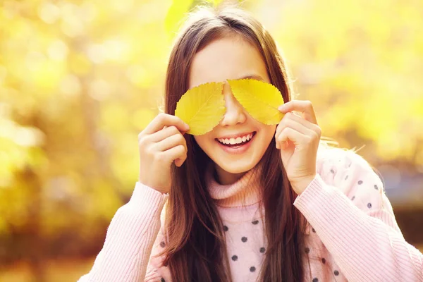 Retrato de cerca de una hermosa adolescente sonriente con hojas amarillas en otoño . —  Fotos de Stock