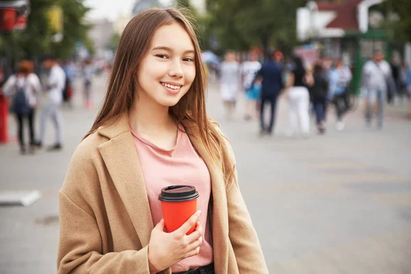 在城市街道的纸杯里喝着饮料的年轻女子。女孩与咖啡去. — 图库照片