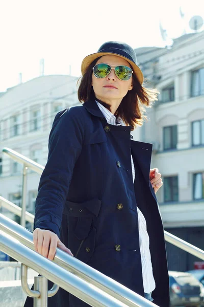 Наружный портрет стильной женщины в плаще, шляпе и солнцезащитных очках. — стоковое фото