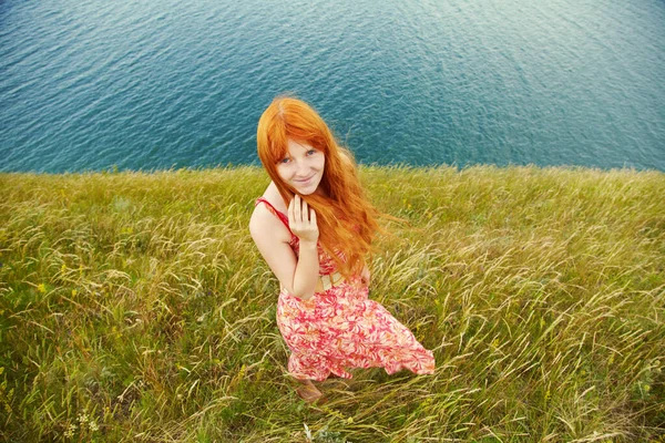 Romantische rothaarige junge Frau in einem Kleid an der Küste. Mädchen im Sommer im Freien. — Stockfoto