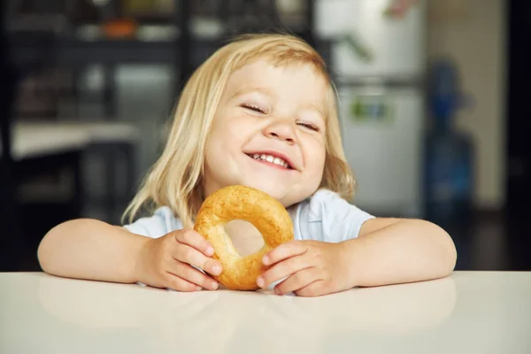 Portret van een grappig meisje met bagel. kind dat thuis speelt. — Stockfoto
