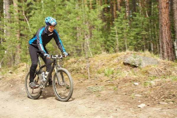 Ciclista montando una bicicleta de montaña a lo largo de la carretera forestal . — Foto de Stock