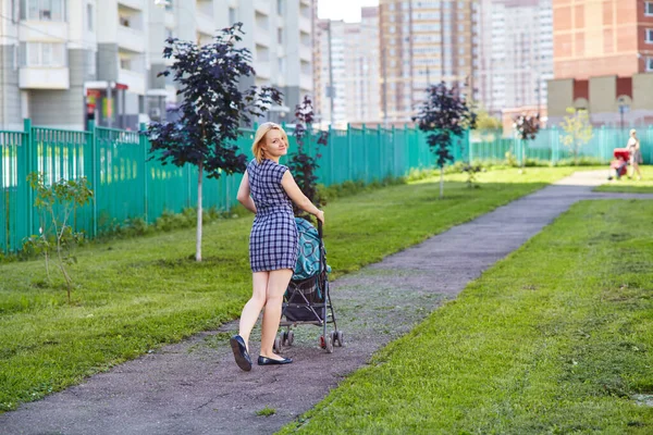 Junge Mutter, die mit einem Baby im Kinderwagen geht. Mutter und kleine Tochter. — Stockfoto