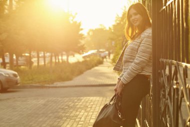 Gün batımında bir şehir sokağında el çantasıyla gülümseyen güzel bir kadının portresi.