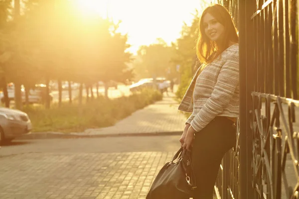 Portrait of a beautiful smiling stylish woman with handbag in a city street on sunset — Stock Photo, Image