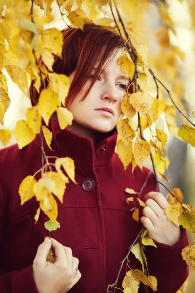 Porträtt av en sorgsen rödhårig kvinna med gula löv på hösten. — Stockfoto