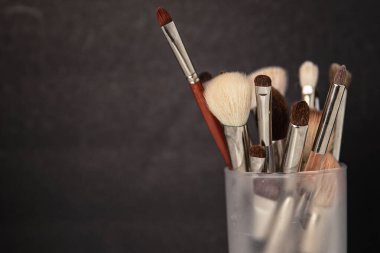 Makyaj Fırçaları Siyah arka planda cam bir bardakta düzenlenmiş bir Vanity üzerinde.