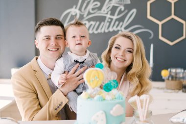 Güzel anne ile birlikte bir yaşındaki çocuklarının evde güzel bir iç şenlikli bir mavi pasta ile pastel renklerde gülümse. Aile bak. Mutlu Doğum günü partisi