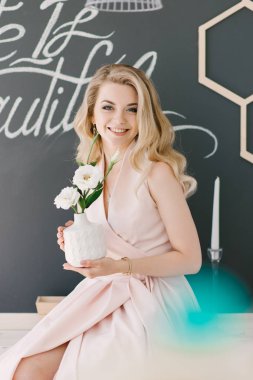 Kıvırcık sarı saçlı güzel bir genç kız portresi. Oturur evde güzel bir iç mekan ve gülümsüyor