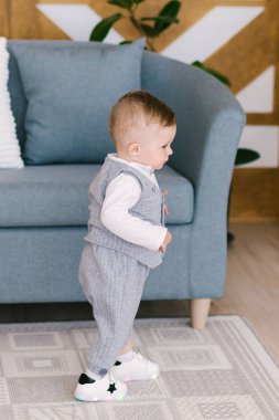 Bir beyefendinin elbiseli mutlu sevimli çocuk hafif bir arka plan üzerinde destek yakınındaki, almaya çalışırken yürümeyi öğrenme standları.