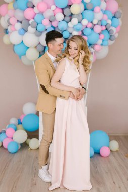 Sarılma ve beyaz ve pembe balonlar arka plan üzerinde gülümseyen güzel bir sarışın kız ile güzel bir genç adam. Sevgi dolu çift, aşk hikayesi