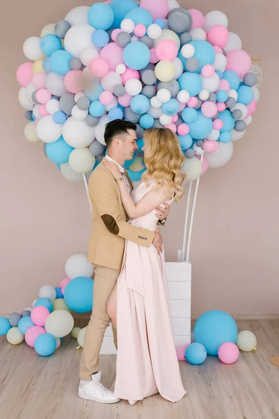 A beautiful young guy with a gorgeous blonde girl hugging and smiling on the background of white and pink balloons. Loving couple, love story