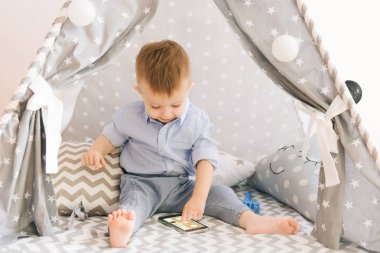 Bir çadır, akıllı telefonlar ile oynarken şirin bir yaşında bebek KızıIderili. Alan, doğal ışık gölge derinliği. Çocuk odası iç gridir mavi ve beyaz