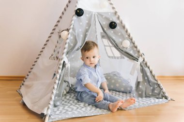 Bir çadırda oynarken şirin bir yaşında bebek KızıIderili. Alan, doğal ışık gölge derinliği. Çocuk odası iç gridir mavi ve beyaz