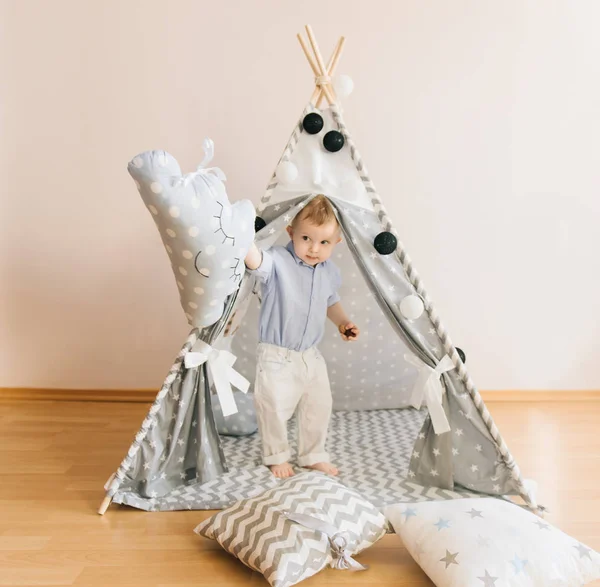 Cute one year old baby playing in a tent, wigwam. Shadow depth of field, natural light. The interior of the children\'s room is grey, blue and white