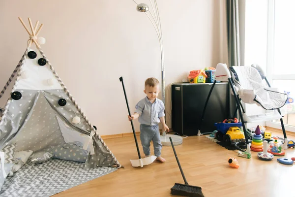 Şirin bir yaşında bebek oda bir süpürge ve teepee yanındaki bir kepçe ile temizler. Alan, doğal ışık gölge derinliği. Çocuk odası iç gridir mavi ve beyaz