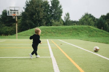 Yapay çim üzerinde futbol topuyla oynayan sevimli bir yaşındaki çocuk