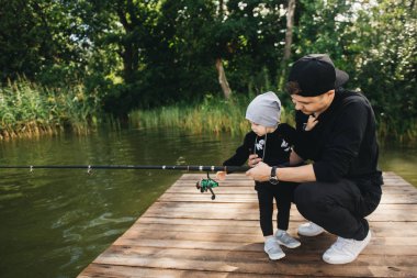 Baba ve sevimli bir yaşındaki oğlu doğada bir olta ile Balık tutma. Kırsal kaçış kavramı. Balıkçılık gün hakkında makale.