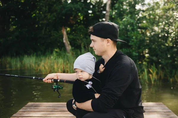 Father and cute one-year-old son fishing with a fishing rod in nature. The concept of rural getaway. Article about fishing day.