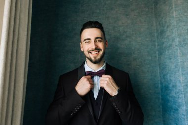 Şık damat beyaz gömlek ve papyon pencere ışıkta poz. Kendinden emin ve mutlu adam portresi. Damat sabah hazırlanıyor. Yaratıcı düğün fotoğraf 