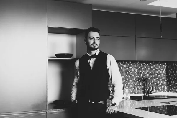 Stylish groom in white shirt and bow tie posing at window light. Confident and happy portrait of man. Groom getting ready in morning. Creative wedding photo
