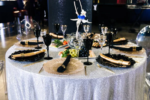 Tables set for an event party or wedding reception. luxury elegant table setting dinner in a restaurant. Black and gold glasses and dishes.