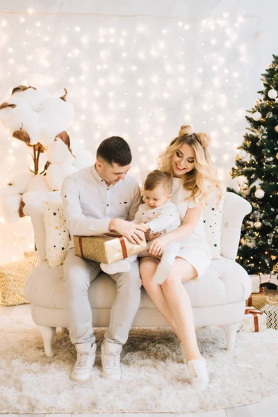 美丽的年轻家庭的肖像上的圣诞树和白色棉背景 有吸引力的父母和一个小儿子打开新年礼物 — 图库照片