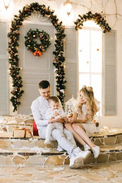 Happy young family sitting on the porch of the house decorated for Christmas. Laugh and prepare for the holiday