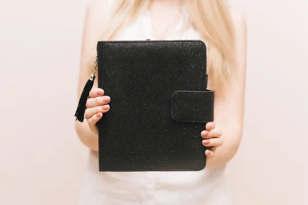 Stylish black notebook with a brush and a button in the hands of the girl. Free space for logo