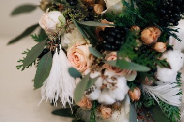 Pastel kış gelinin buket gül ile Ladin, pamuk, siyah meyveleri, tüyler ve kurutulmuş çiçeklerin renkleri. Küpe ile tüyleri mi. rustik bir buket üzerinde. Seçici odak