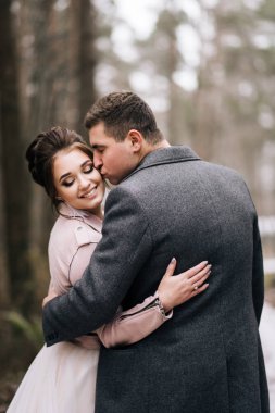 Genç ve mutlu bir çiftin portresi. Damat gelini orman yolunda öpüyor. Düğün günü.