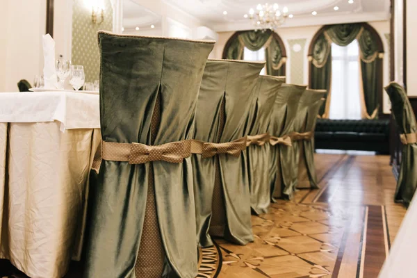 Decorated chairs. Silk bow tied on back of chair in party at restaurant. Dark cloth cover chairs standing in a row