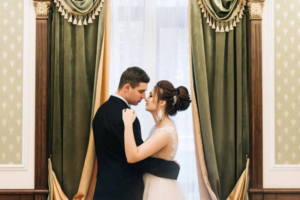 窓の近くの豪華なインテリアで新郎新婦の幸せな若い恋人たちの肖像画 結婚式の日 — ストック写真