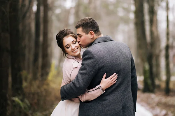 幸せな若い愛する新婚旅行の肖像画 新郎は森の路地で花嫁にキスをします 結婚式日 — ストック写真