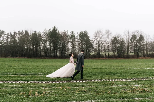 Portrait of happy young loving newlyweds.  The bride and groom run across the field with the first snow. Wedding day