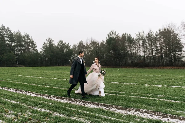 快乐的年轻有爱心的新婚夫妇的肖像 新郎新娘带着第一场雪跑过田野 婚礼当天 — 图库照片