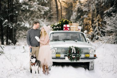 Bir adam ve bir kız Noel, eski model araba, çatı ağaç ve hediyeler karlı kış ormandaki bir arka plan üzerinde husky köpek yürüyüş için hazırlık