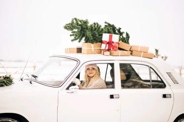 Kız bir Noel ağacı ile dekore edilmiş bir retro araba sürmek ve karlı bir ormanda sunar. Kış Noel fotoğrafını kavramı ateş