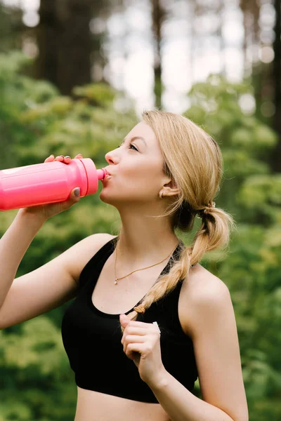Beautiful young girl in sports uniform with a bottle of water doing yoga and sports in the forest in the open air