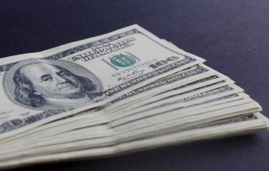 Karanlık bir arka plan üzerinde yüz dolarlık banknot yığınını kapatın.
