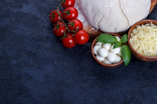 Pizza margherita ingridients çiğ hamur kiraz domates fesleğen zeytinyağı mozzarella peyniri karanlık taş mutfak masasında 